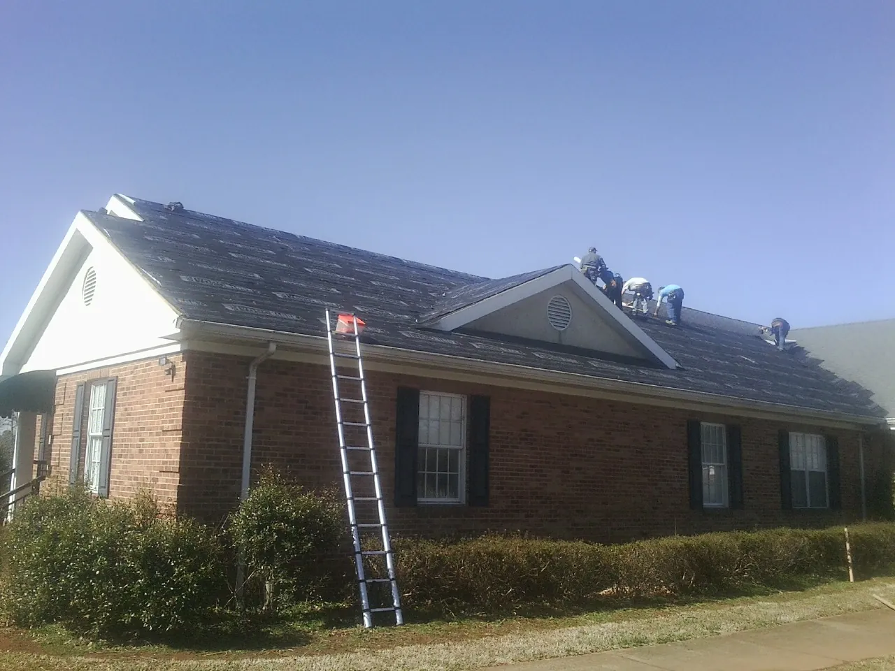 Crew tearing shingles off a brick ranch roof with a ladder set — Emergency Roof Repair work by our crew in Romulus