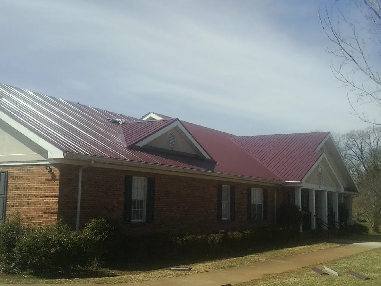 Red metal roof with gabled entries on a long brick building, from a Hail Damage Roof Repair job in Romulus