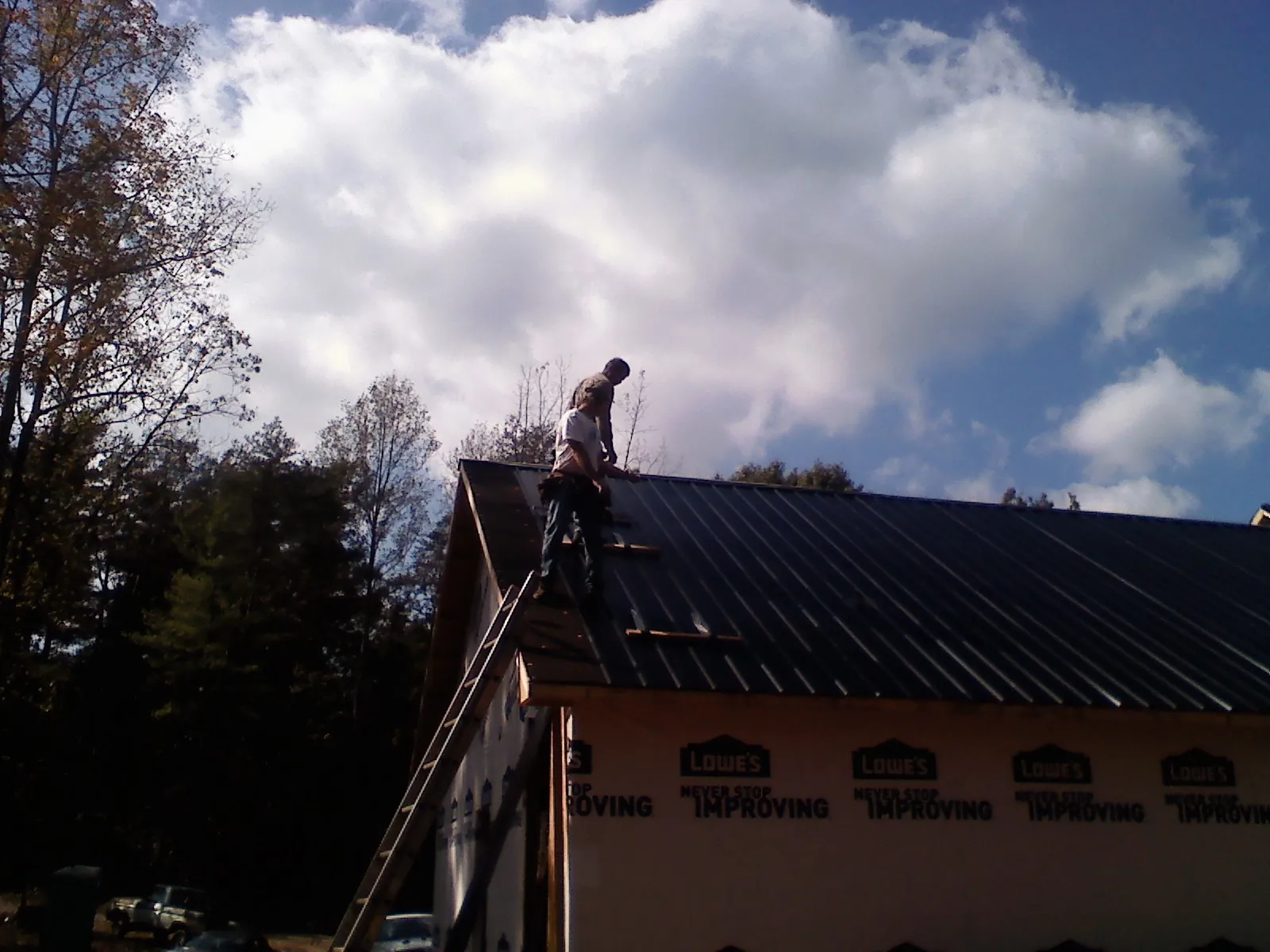 Roofer fastening dark metal panels high against a cloudy sky in Romulus