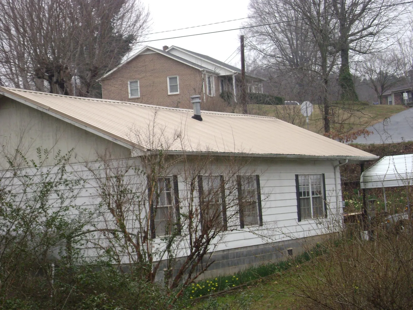 Tan metal roof on a white sided house set into a hillside — Commercial Roofing by Roofing Brothers in Romulus