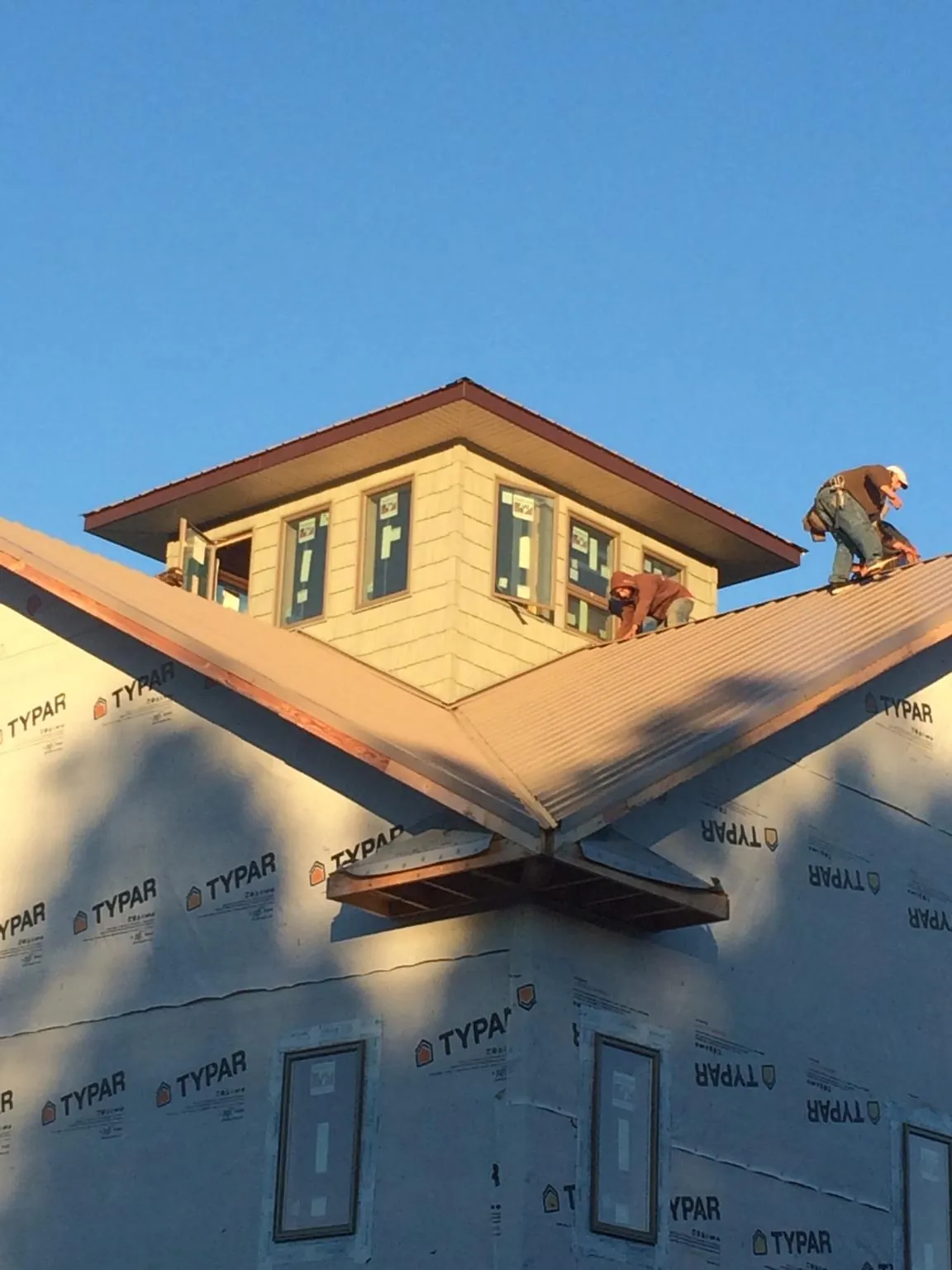 Roofers working around a rooftop cupola on a new metal roof at sunset — Roof Waterproofing in Romulus by Roofing Brothers